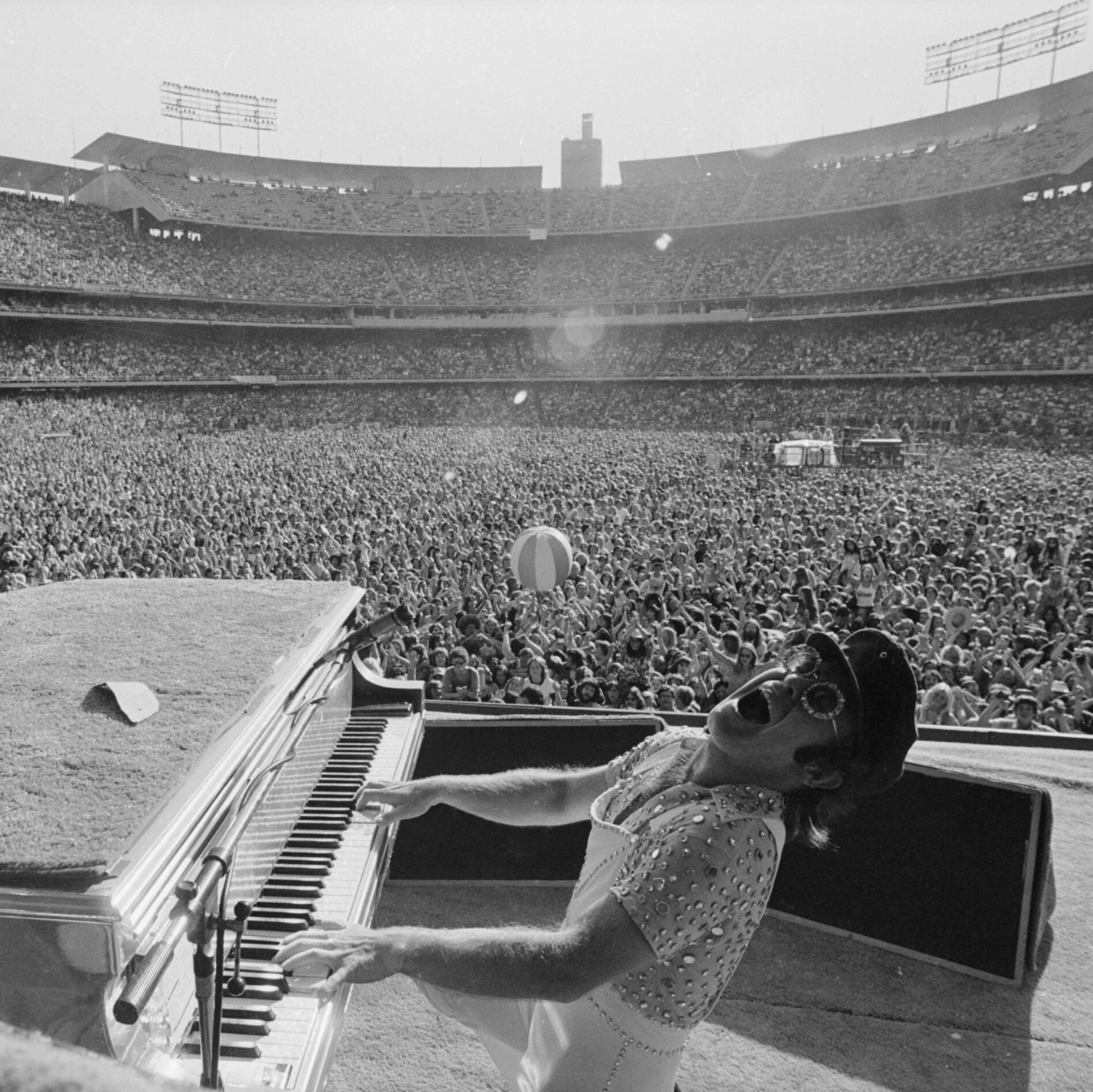Elton John vid ett piano på en scen inför en fullsatt arena 