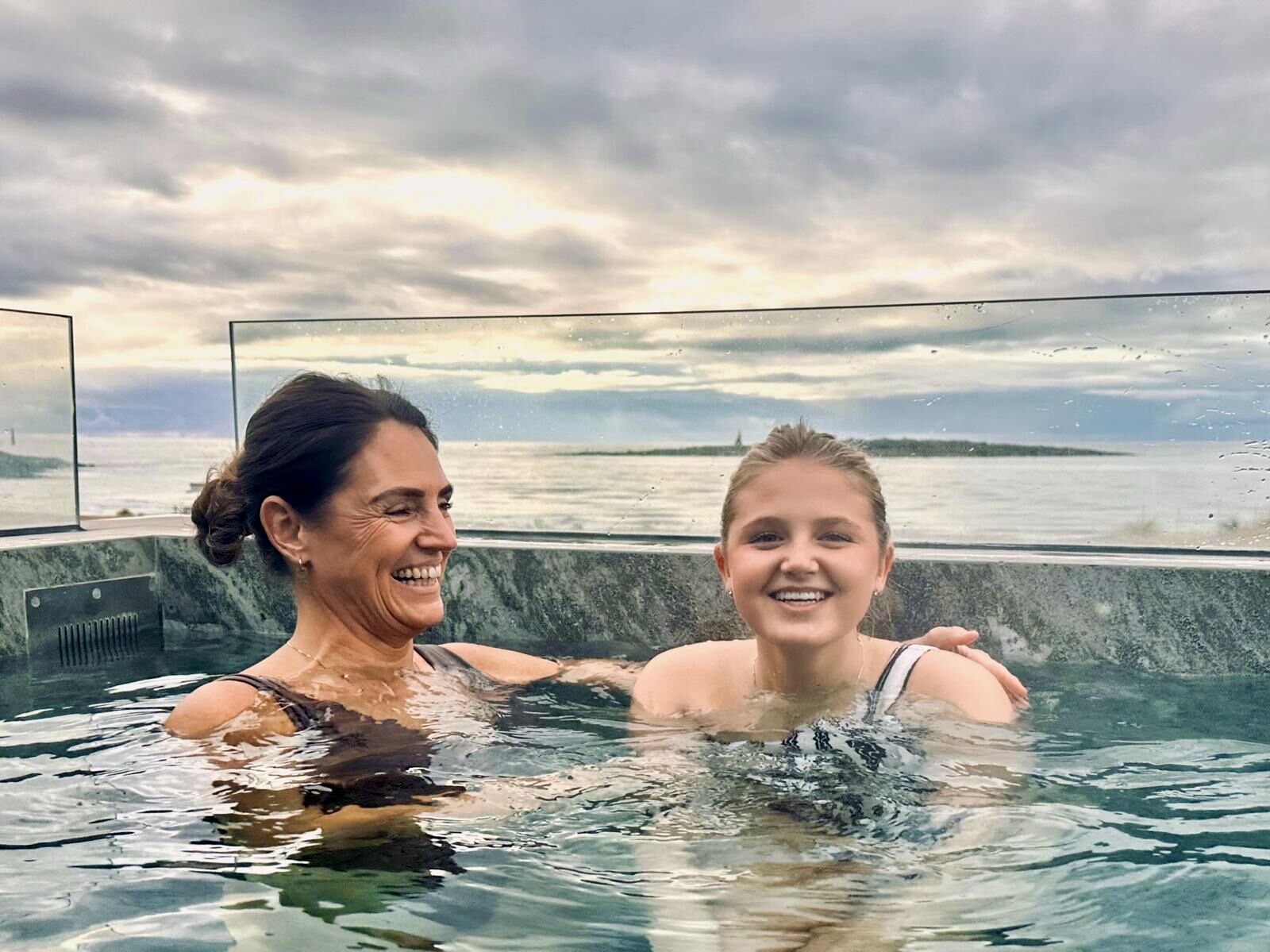 Mamma och dotter i spapool med havsutsikt.