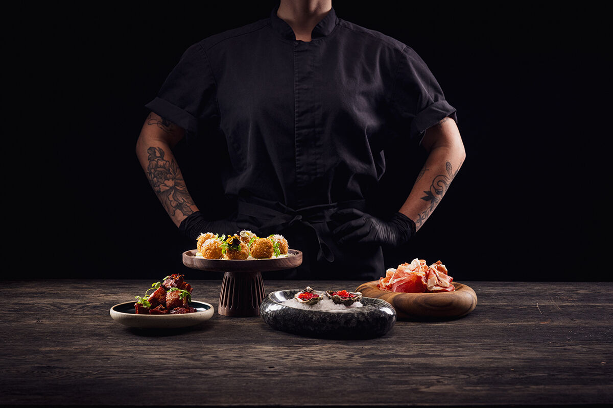 En kvinnlig kock står bakom fyra olika maträtter.