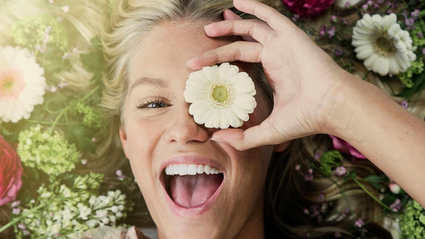 En glad tjej håller en blomma framför ena ögat.