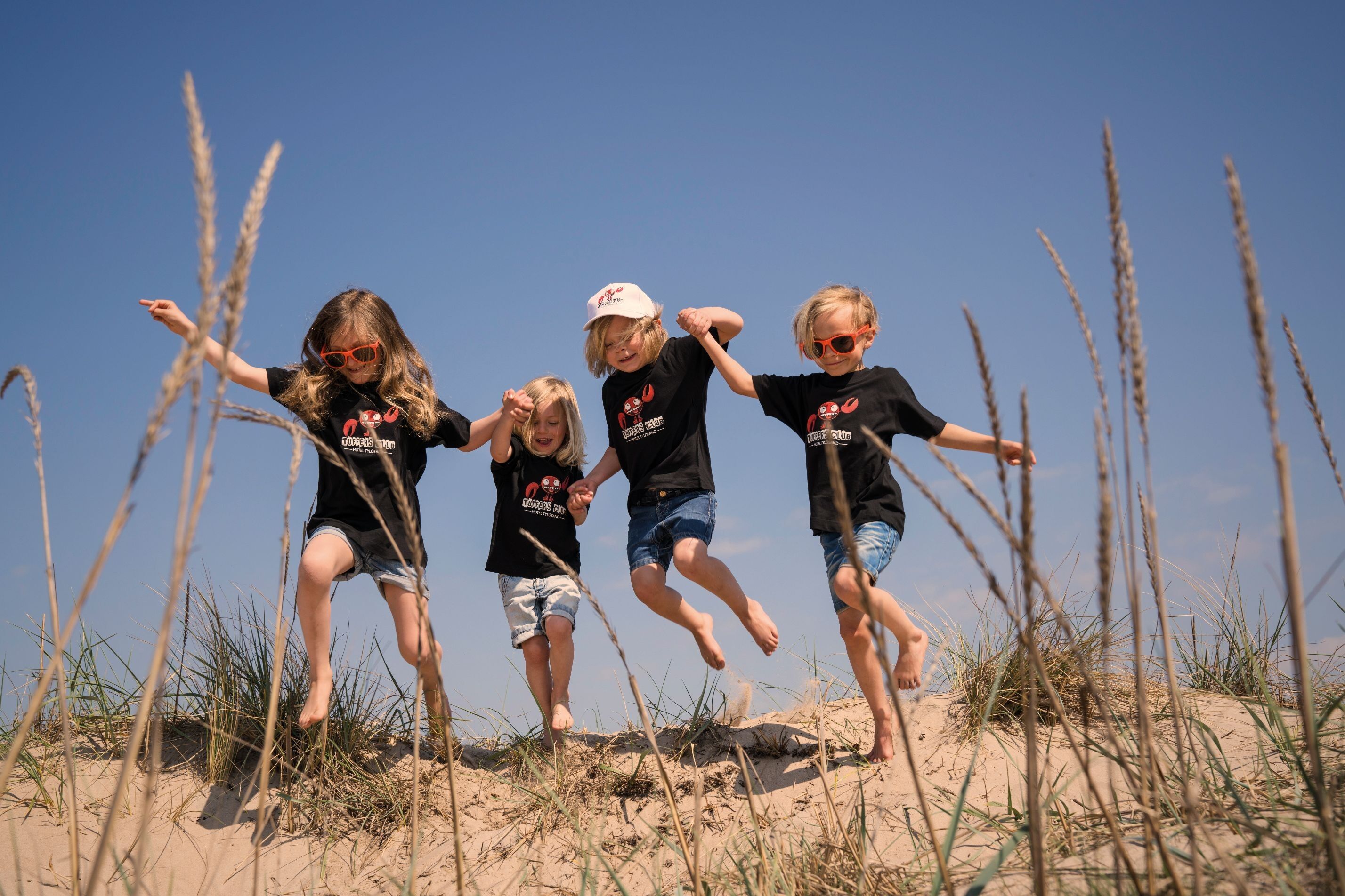 Fyra barn som springer hand i hand på sanddynerna på Tylösand s